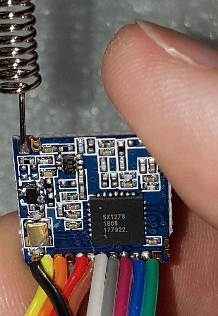 A LoRa transceiver module with whip antenna and SPI flying leads. Functionally equivalent topology to the RFM95W: SX127x family transceiver, 100 mW TX, FSK or LoRa modulation.