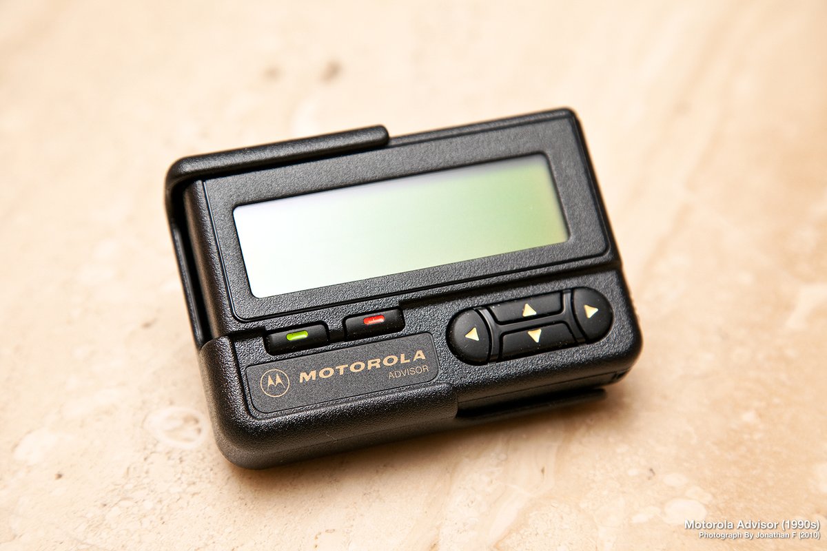 A Motorola Advisor pager — the donor shell for the Kelly Pwnagotchi mod. The clamshell flips open; the inside of the lid carries the LCD aperture; the top-edge rocker handles navigation. The versio…
